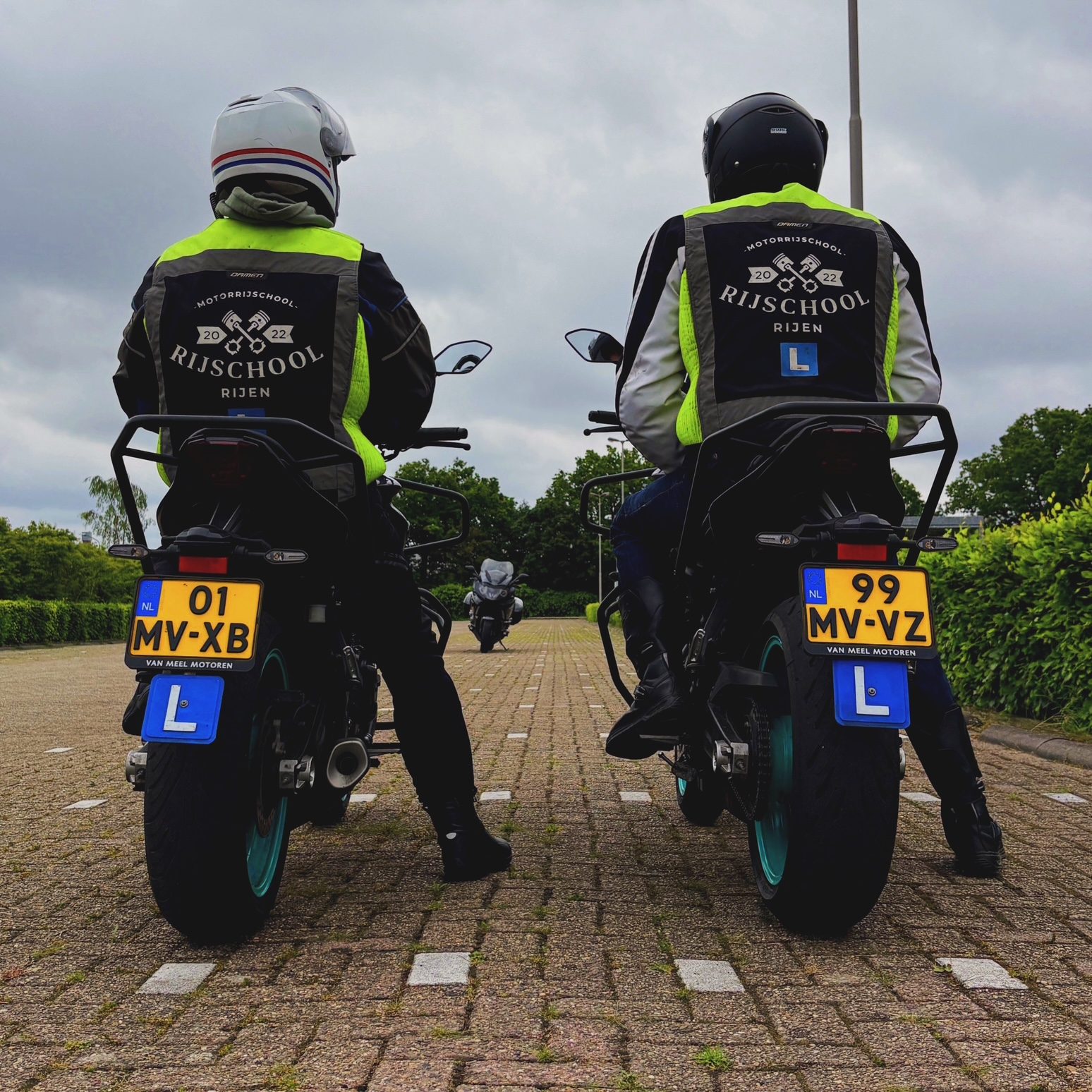 Twee leerlingen in Rijschool Rijen-hesjes op hun lesmotor, klaar om te vertrekken, van achteren gezien