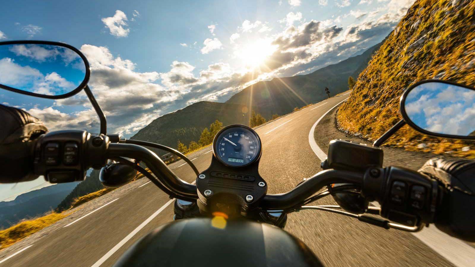 Zicht over het stuur van een motor op een bochtige bergweg in de zon