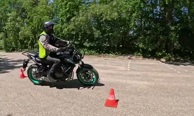 Leerling in een geel hesje rijdt op de lesmotor langs de pionnen op het oefenterrein
