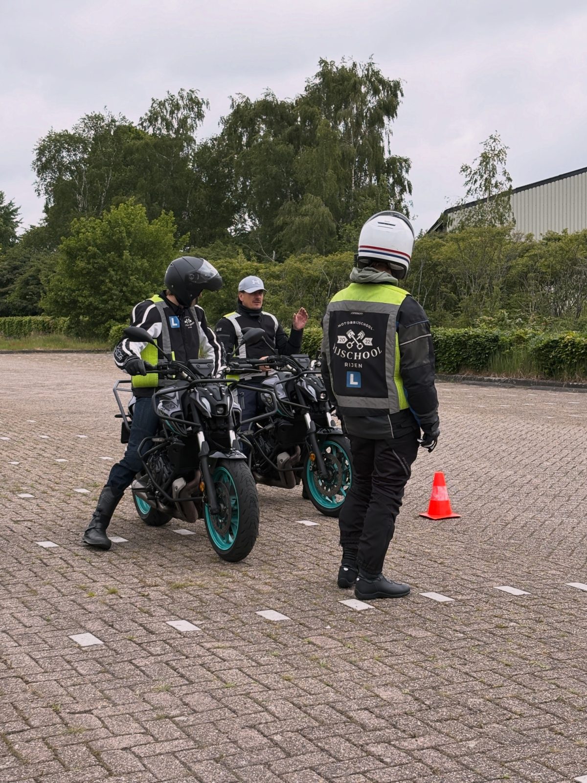 Instructeur geeft uitleg aan twee leerlingen op hun lesmotor op het oefenterrein